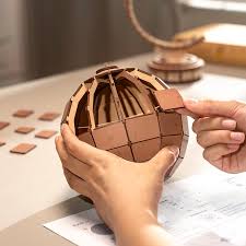 Person assembling a 3D astronomical globe wooden puzzle on a desk with a lamp in the background