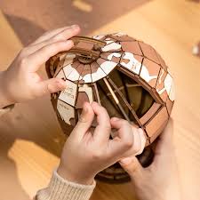 Person assembling a metallic, 3d astronomical globe puzzle with intricate design