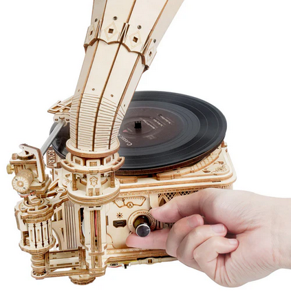 Wooden mechanical model of a record player with a hand interacting with it on a white background