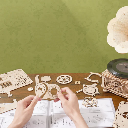 Person assembling wooden mechanical models on a table with a green wall background