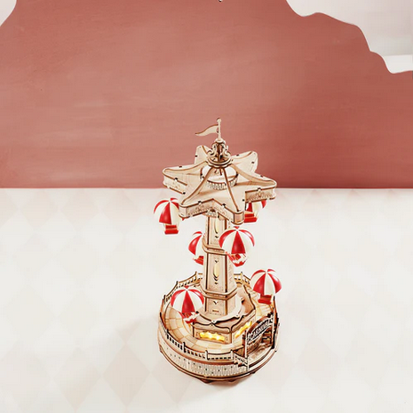 Decorative model of a carousel with red and white striped umbrellas on a light pink background