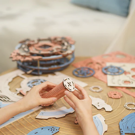 Hands holding a wooden craft tool over a table with puzzle cutouts